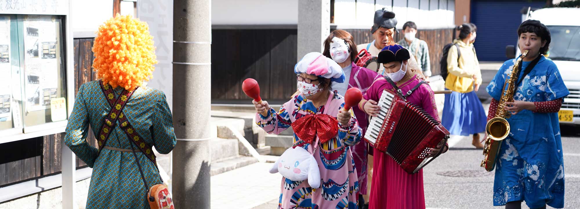 まちなかをアフロのカツラや帽子をかぶった派手な衣装の人たちが楽器を持って練り歩いている写真