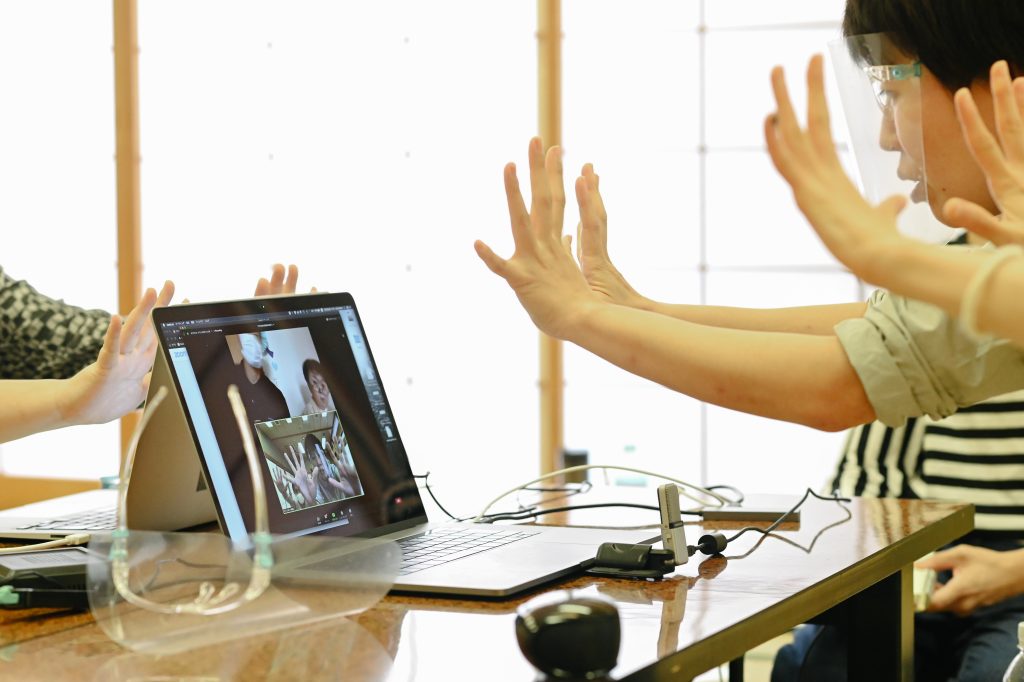 2人のアーティストがノートパソコンの画面に映っている参加者に向かって手を伸ばしている様子